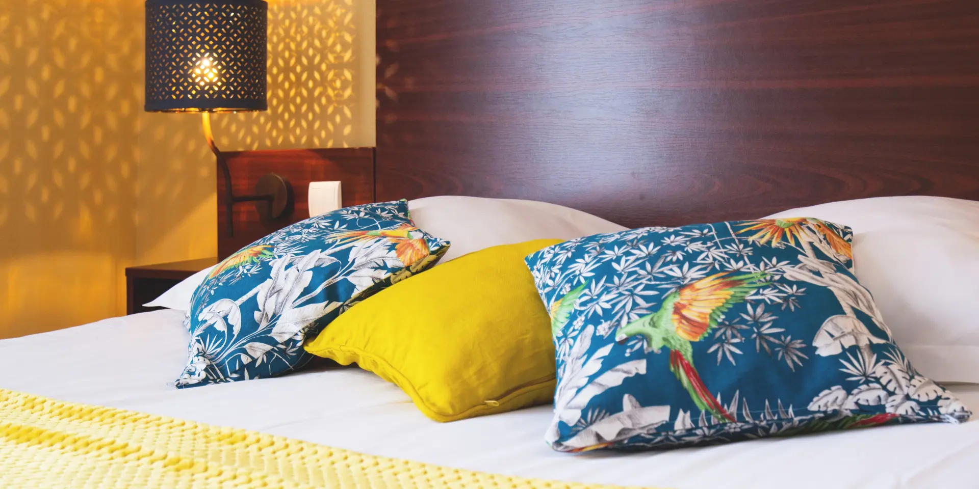 Hotel bed with blue and yellow wave-patterned blanket under soft lighting