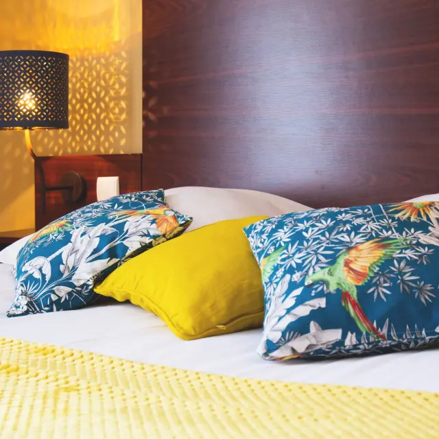 Lit d'hôtel avec couverture à motifs de vagues bleues et jaunes, sous une lumière tamisée