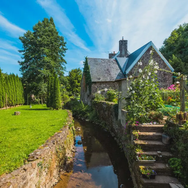 Moulin à vent en pierre avec des ailes en bois, situé au bord d’un canal bordé de verdure