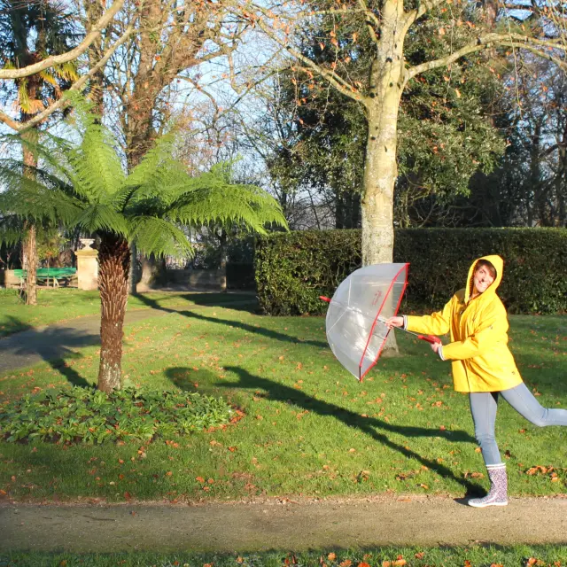 Femme en imperméable jaune tenant un parapluie transparent dans un parc