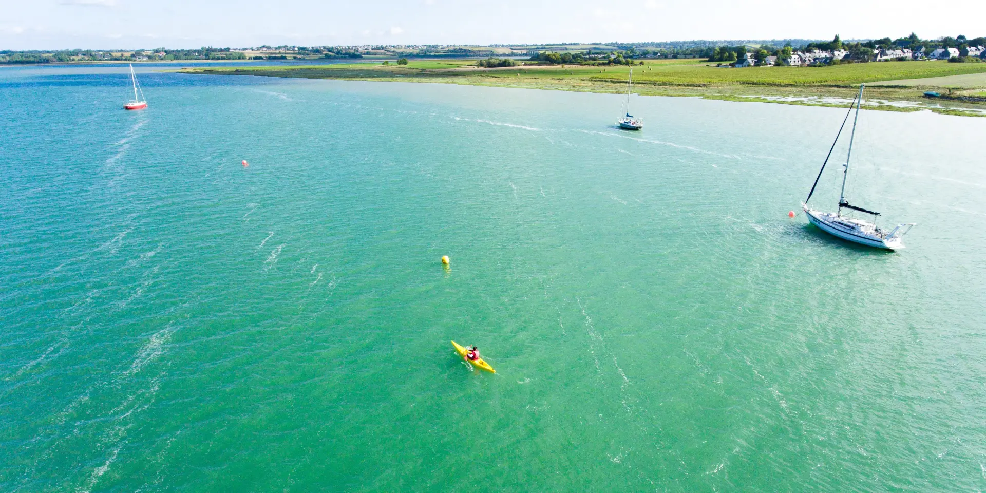 Person in a yellow kayak on a turquoise sea with sailboats