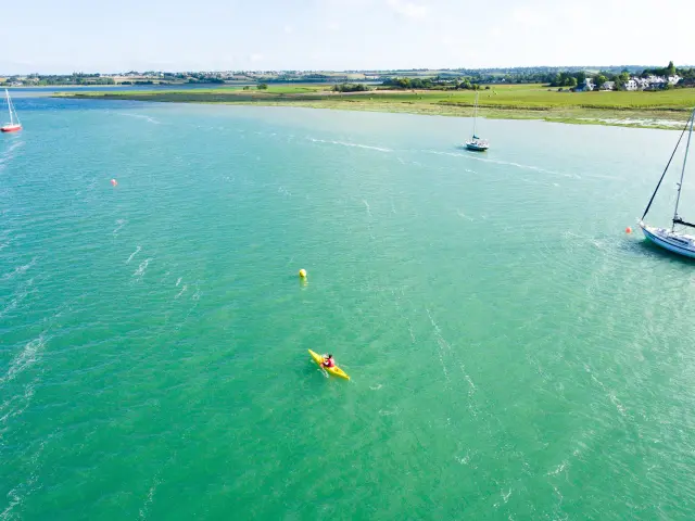Personne en kayak jaune sur une mer turquoise avec des bateaux à voile