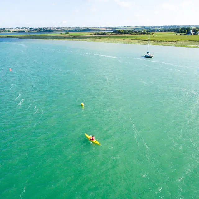 Person in a yellow kayak on a turquoise sea with sailboats