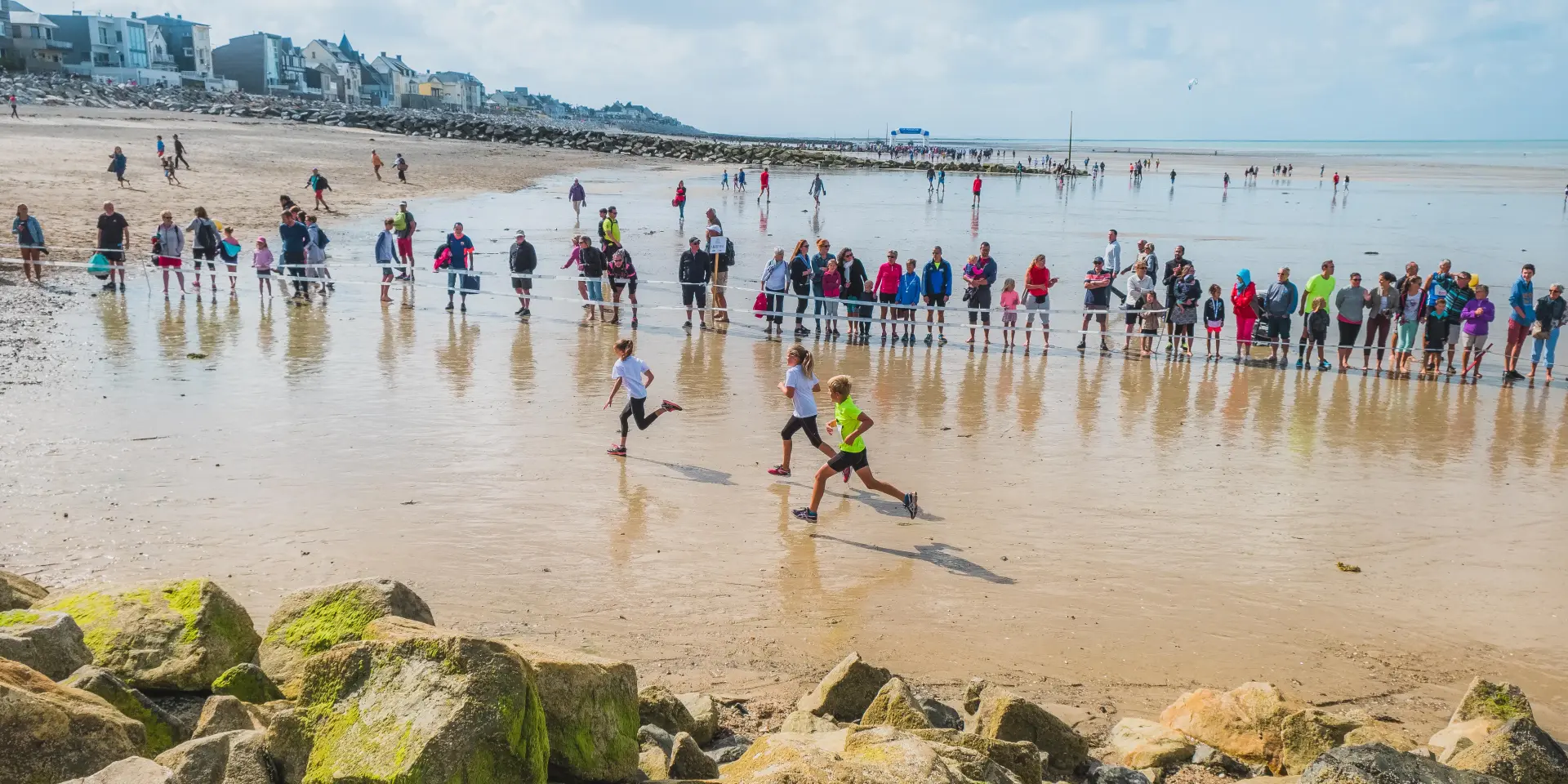 Plage avec des personnes jouant au frisbee et des voiliers amarrés en arrière-plan