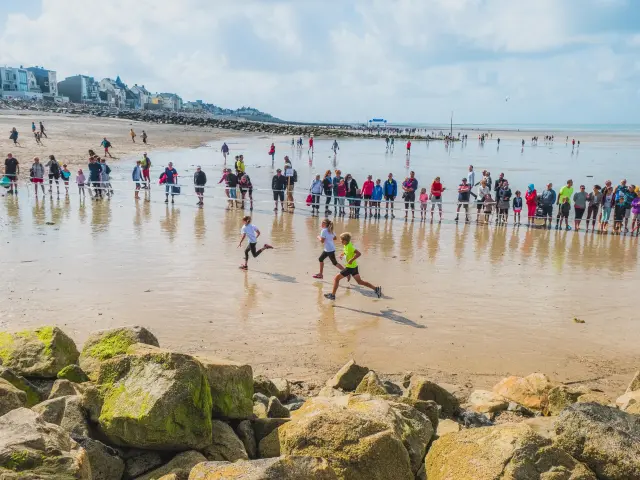 Strand mit Personen, die Frisbee spielen, und vertäuten Segelbooten im Hintergrund