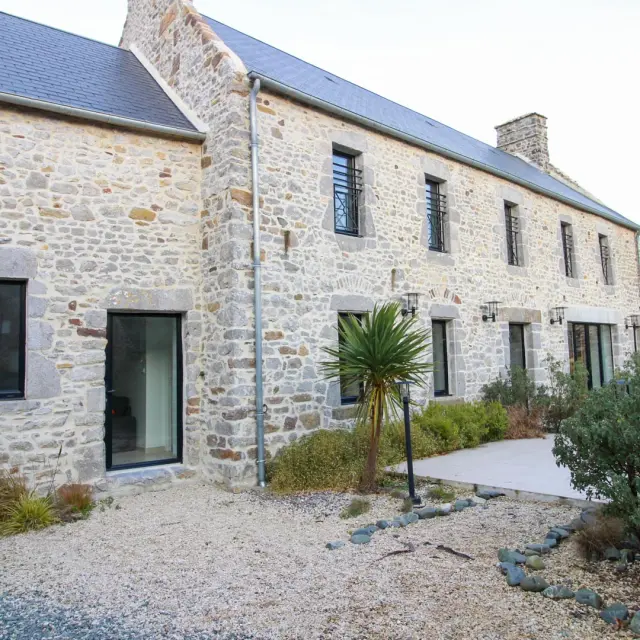 Steinhaus mit großen Fenstern und landschaftsgestaltetem Garten