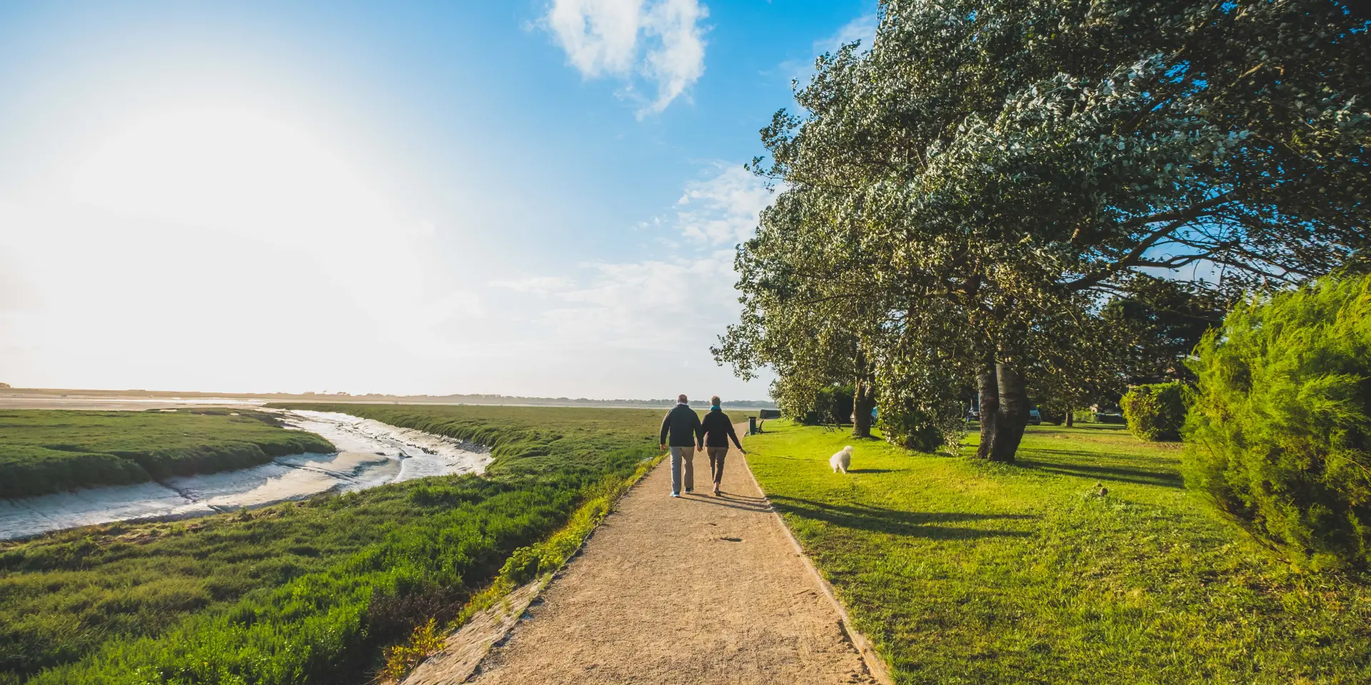 Two people walking on a dirt path near a body of water