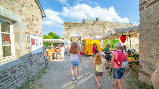 Menschen, die durch einen historischen Markthof mit Ständen und Steinbauten gehen