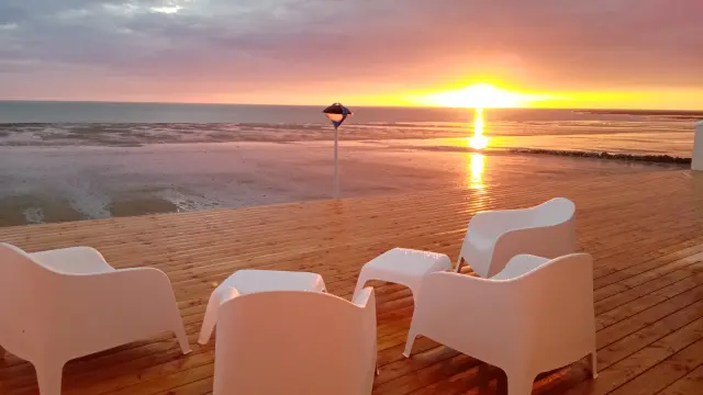 Weiße Stühle auf einer Holzterrasse mit Blick auf das Meer beim Sonnenuntergang