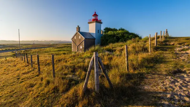 Phare rouge et blanc avec une antenne sur un terrain herbeux en bord de mer