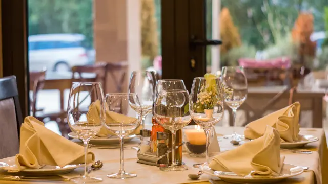 Table de restaurant en terrasse avec verres à vin, bouteilles et plats préparés, vue sur un plan d'eau