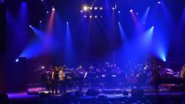 Scène de concert avec musiciens sur scène éclairés par des projecteurs bleus et des lasers