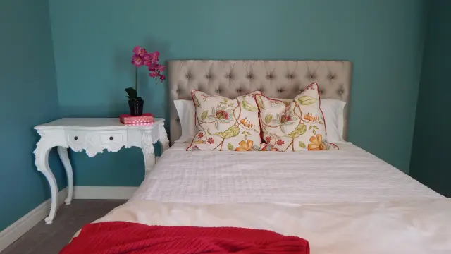 Chambre d'hôtel avec lit double recouvert d'une couverture à motifs floraux, table de chevet et lampe