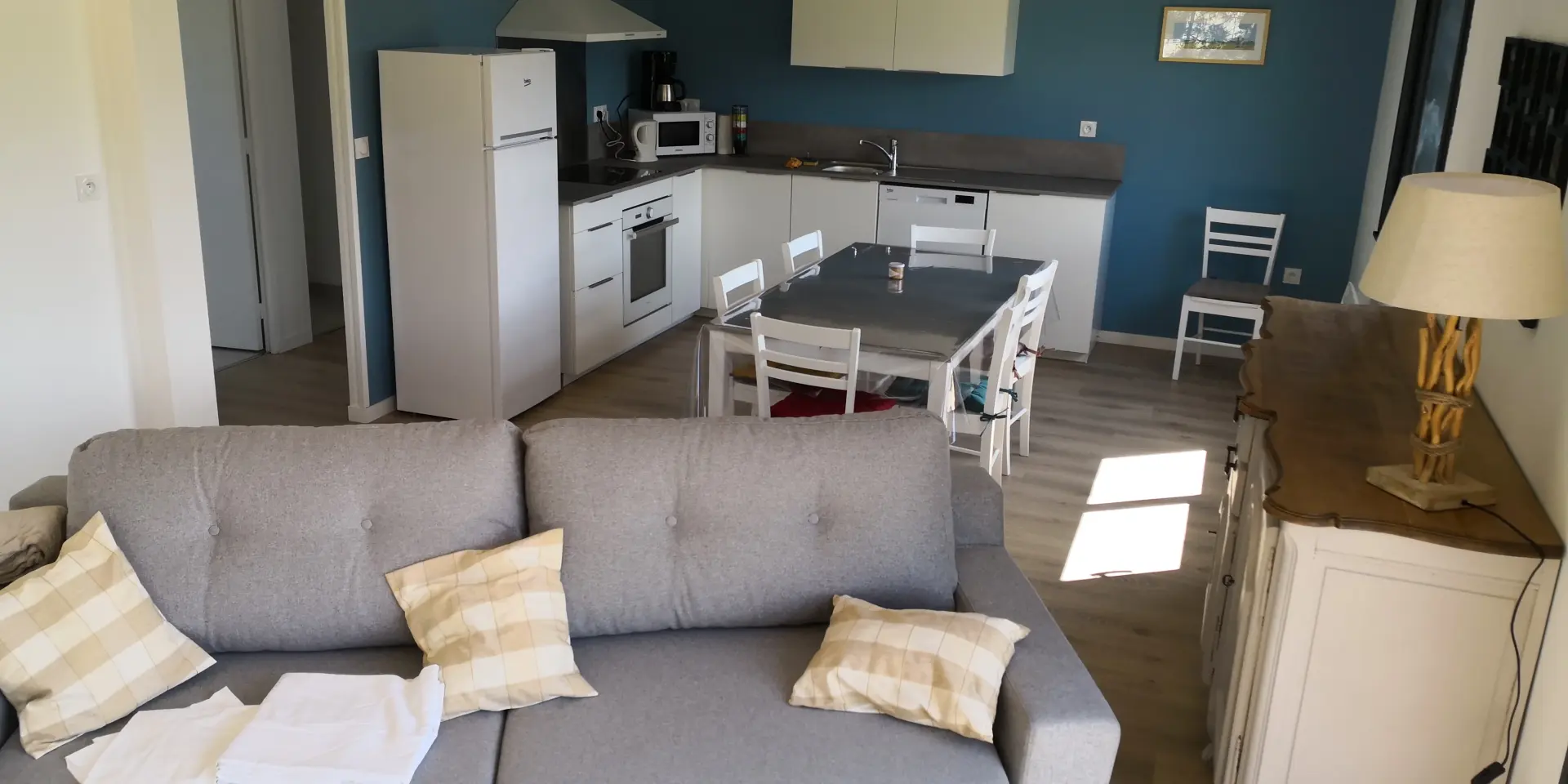 Modern interior with kitchen and living room, gray sofa with pillows, dining table and chairs