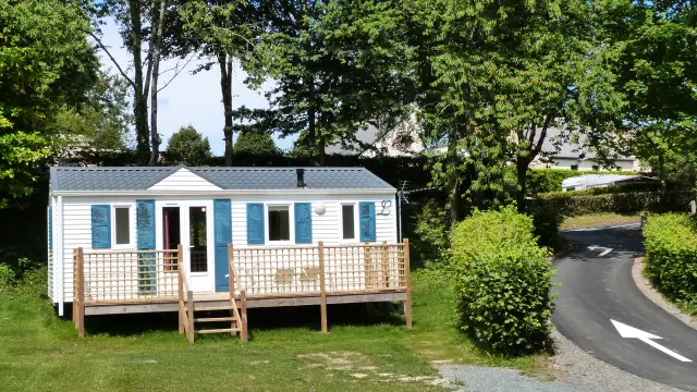 Petite maison en bois avec véranda, entourée d'arbres et d'une allée en gravier