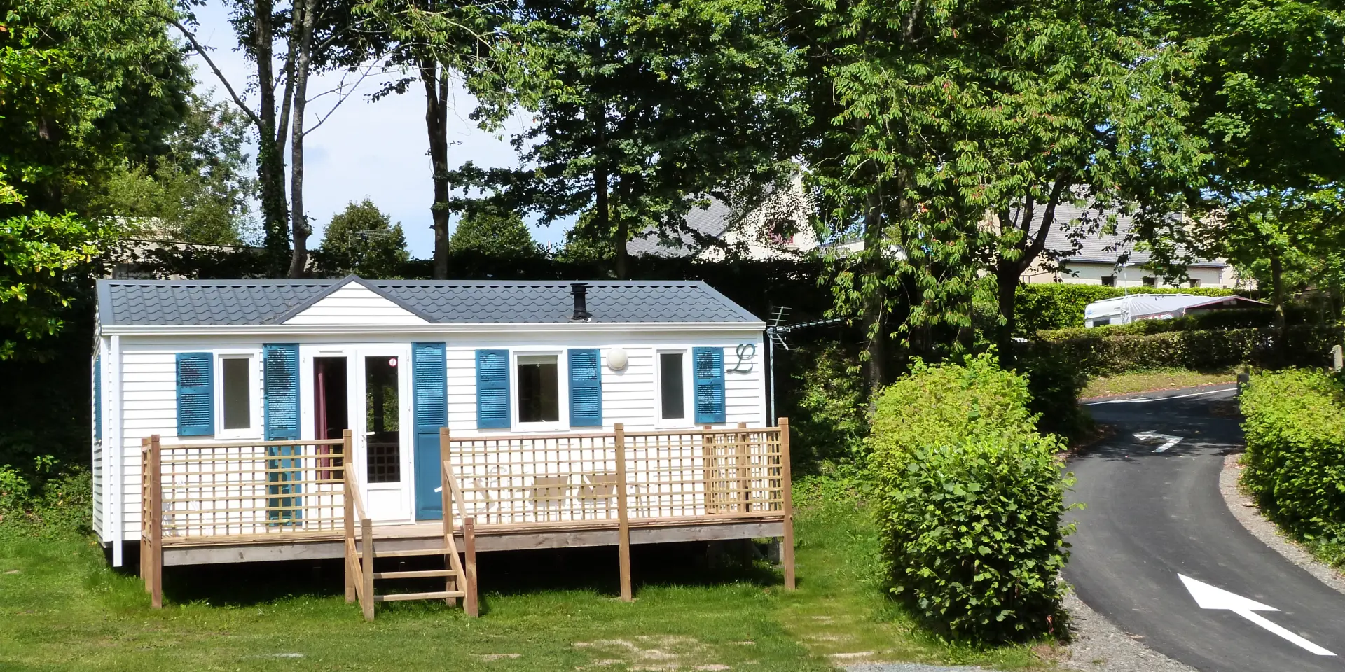 Petite maison en bois avec véranda, entourée d'arbres et d'une allée en gravier