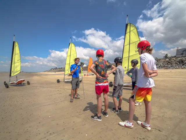 Quatre enfants jouant au beach-volley sur une plage, avec des filets et des drapeaux colorés