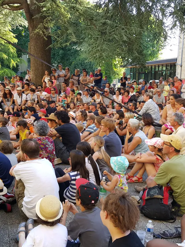 Busy outdoor terrace with people seated around tables under leafy trees