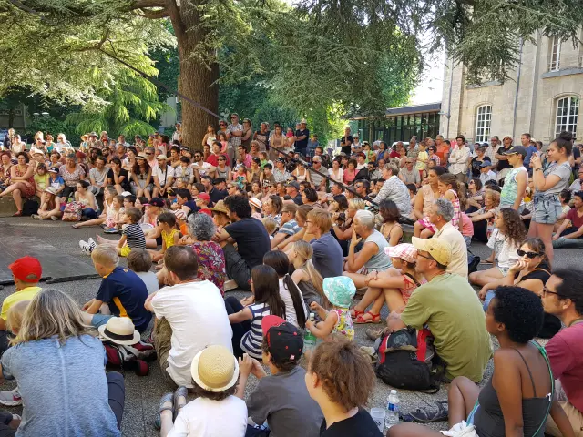 Belebte Außenterrasse mit Menschen an Tischen unter Laubbäumen