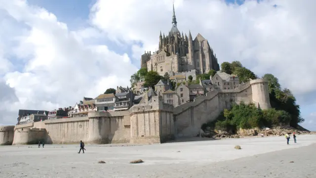 Château fortifié en pierre avec tours crénelées surplombant une plage où des promeneurs sont visibles