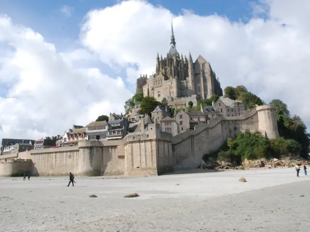 Château fortifié en pierre avec tours crénelées surplombant une plage où des promeneurs sont visibles