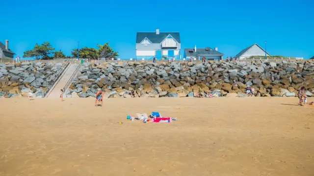 Plage de sable avec des voiliers amarrés, des parasols et des personnes en train de se baigner