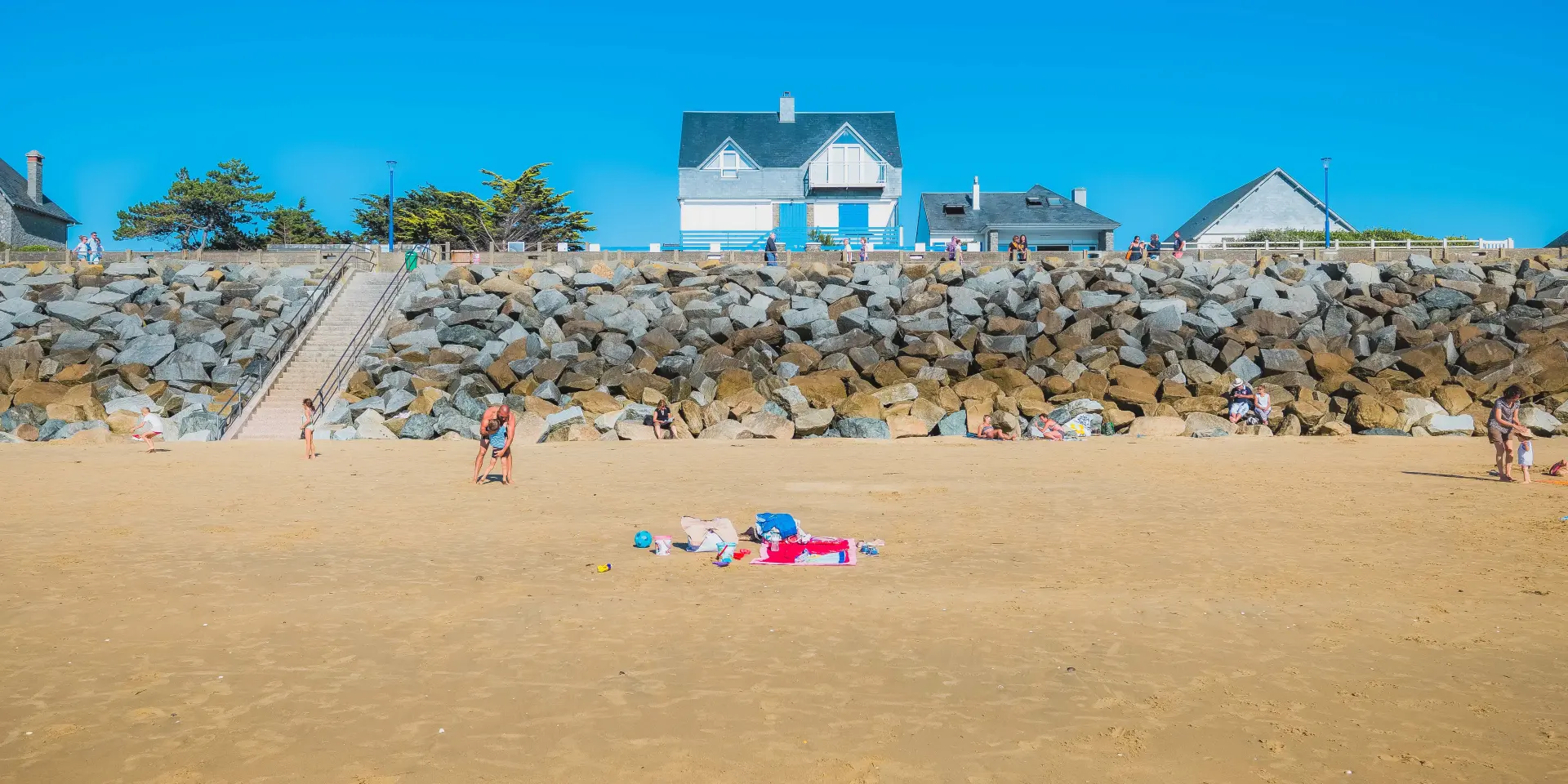Children playing on a beach with a stone seawall and houses in the background