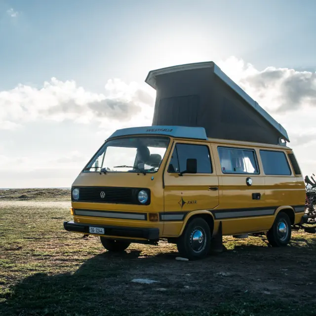 A yellow van with a raised roof is parked on a beach with a bicycle next to it