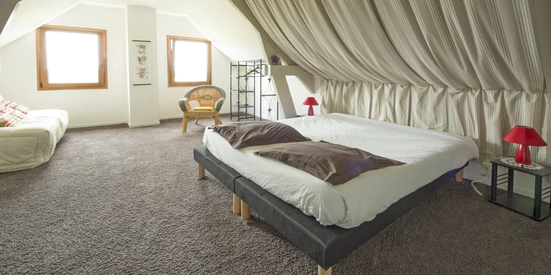 Chambre mansardée avec deux lits, des rideaux blancs et une décoration minimaliste