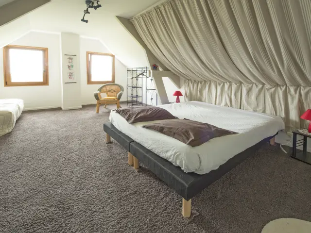 Chambre mansardée avec deux lits, des rideaux blancs et une décoration minimaliste