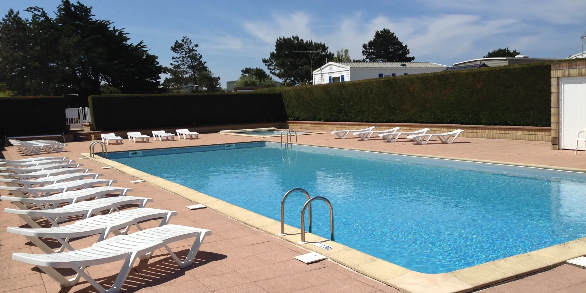 Piscine rectangulaire avec transats alignés et parasols ouverts, entourée de dalles en pierre