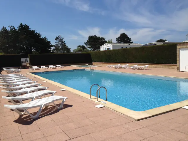 Piscine rectangulaire avec transats alignés et parasols ouverts, entourée de dalles en pierre