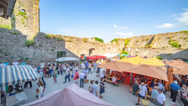 Marché en plein air avec étals colorés et foule de visiteurs sous un ciel bleu