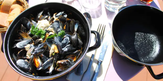 Un pot de moules marinières avec des coquillages ouverts et fermés, accompagné de persil et de pain