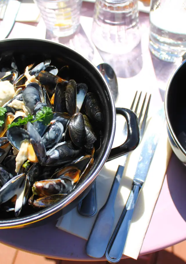 Un pot de moules marinières avec des coquillages ouverts et fermés, accompagné de persil et de pain