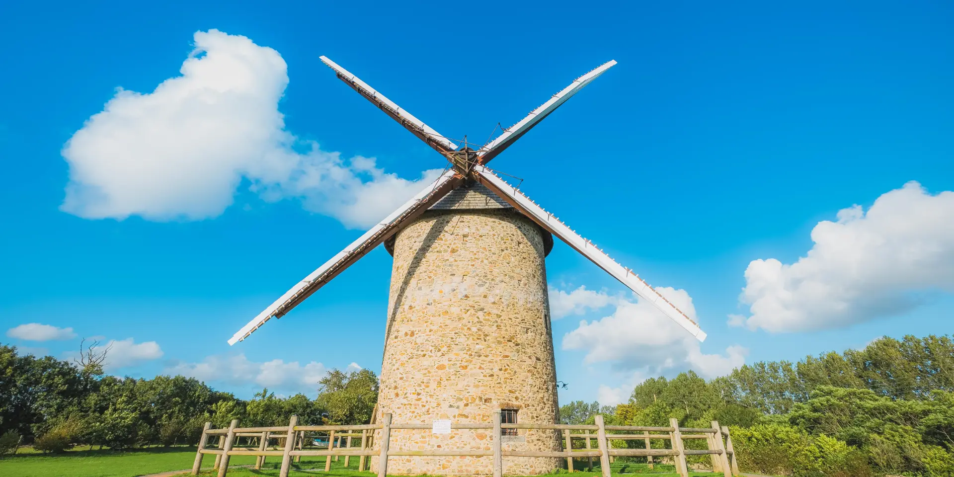 Un moulin à vent en pierre à Gouville sur Mer avec des ailes en bois sous un ciel bleu clair