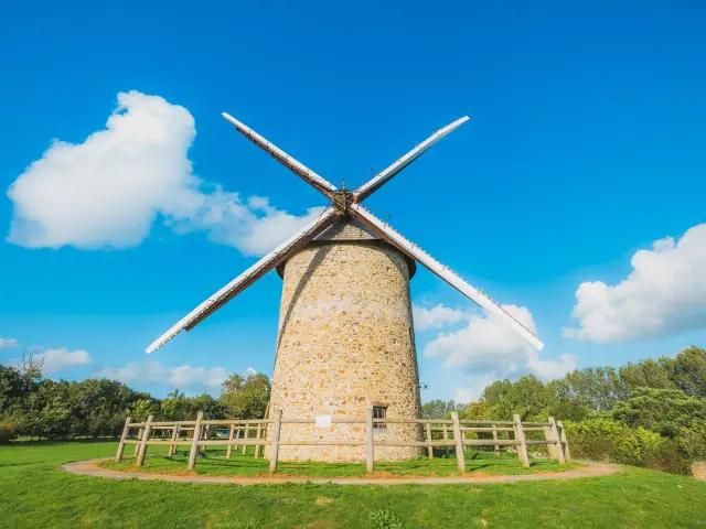 Un moulin à vent en pierre à Gouville sur Mer avec des ailes en bois sous un ciel bleu clair