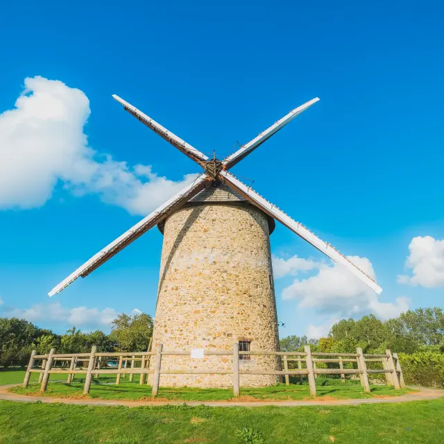 Un moulin à vent en pierre à Gouville sur Mer avec des ailes en bois sous un ciel bleu clair