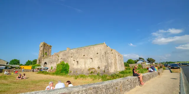 Ruines du château de Regnéville sur Mer avec des gens assis sur un mur de pierre
