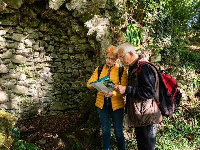 Two elderly people consulting a map near a stone wall in the countryside