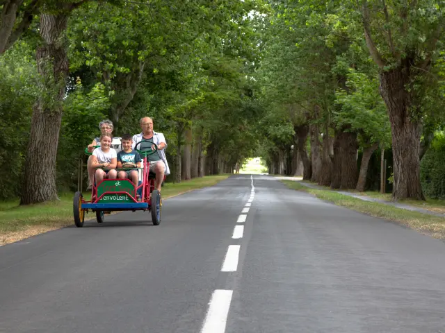 Une famille de quatre personnes sur une rosalie à quatre places sur une route bordée d'arbres à Hauteville sur Mer