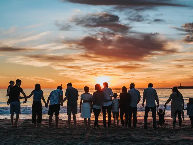 Une grande famille se tient sur une plage au coucher du soleil