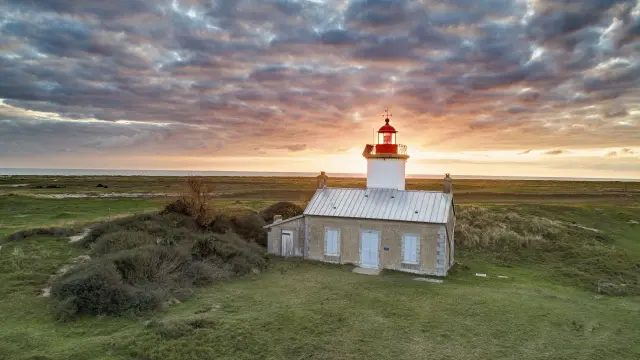 White lighthouse with a red lantern on a grassy hill at sunset