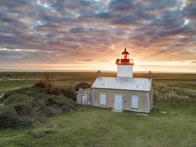 Weißer Leuchtturm mit roter Laterne auf einem grasbewachsenen Hügel bei Sonnenuntergang