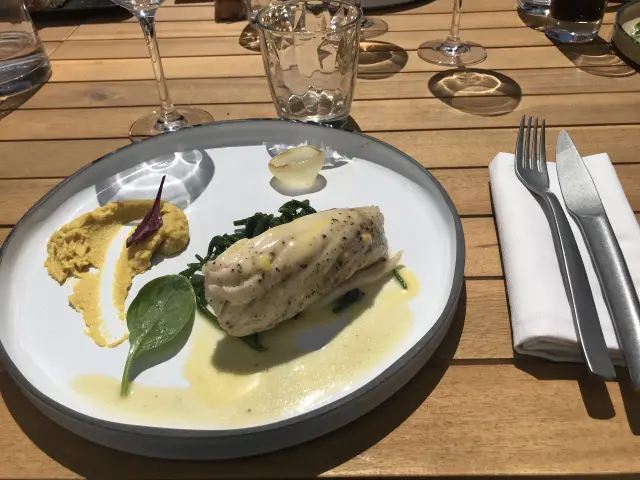 Assiette blanche contenant un filet de poisson grillé, des légumes verts et une sauce blanche, accompagnée d'une fourchette