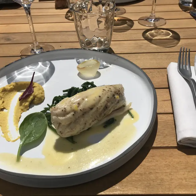 Assiette blanche contenant un filet de poisson grillé, des légumes verts et une sauce blanche, accompagnée d'une fourchette