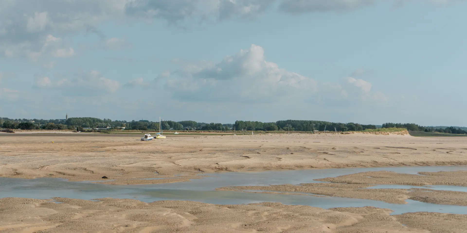 Sandstrand mit Wasserpfützen und bewölktem Himmel