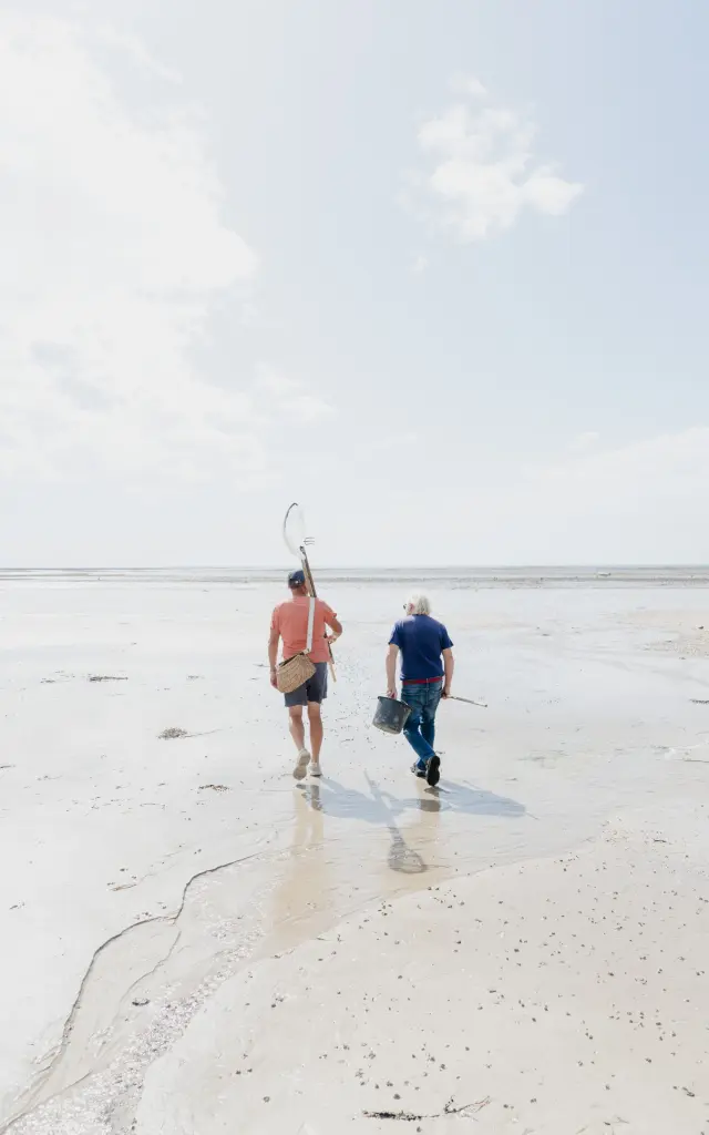 Deux personnes marchant sur une plage de sable avec des filets à de pêche pour la pêche à pied à Agon Coutainville