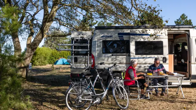 Deux personnes assises devant un camping-car avec des vélos à proximité