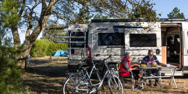 Deux personnes assises devant un camping-car avec des vélos à proximité